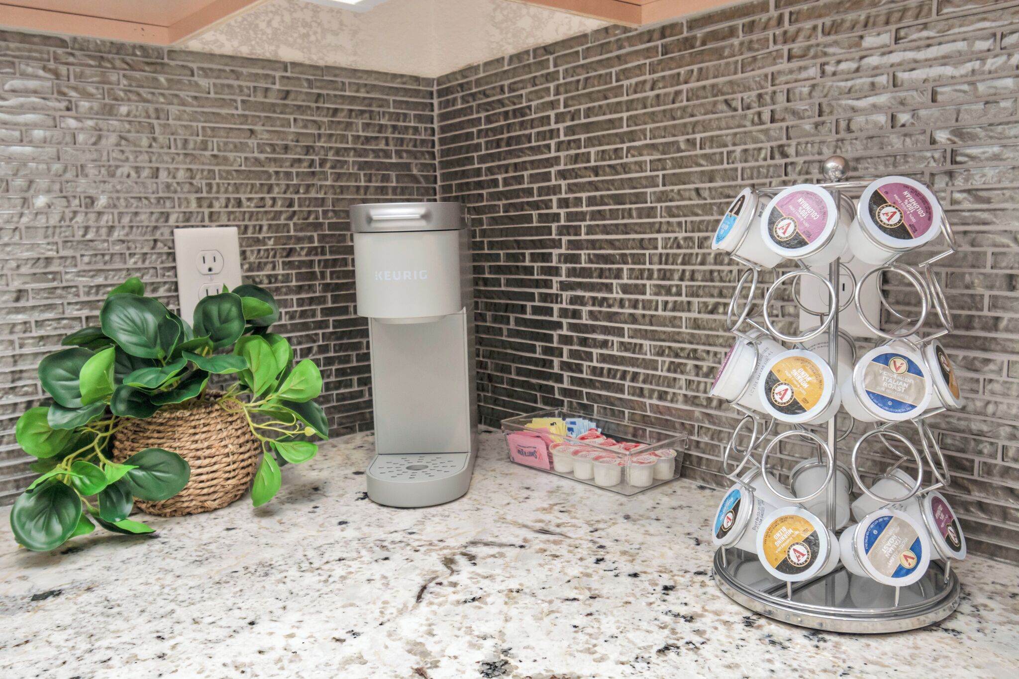 Une cuisine avec un mur recouvert de briques, une machine à café, une plante et un porte-tasses.