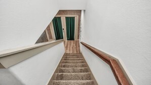 Un escalier avec des marches en bois et une rampe en bois, menant à une pièce dotée d’un rideau vert et d’une porte.