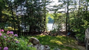 Un jardin paisible au bord du lac, doté d’une terrasse en bois, entouré d’arbres denses et offrant une vue sur le lac.