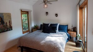 Une chambre à coucher avec un lit, un ventilateur de plafond, une fenêtre et un tableau accroché au mur.