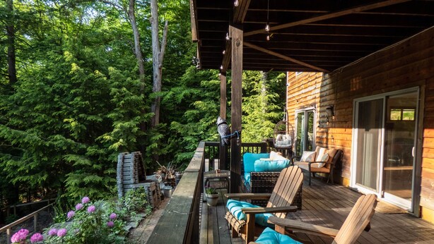 Une terrasse en bois avec des sièges extérieurs, entourée d’une végétation luxuriante et d’un chalet en bois.