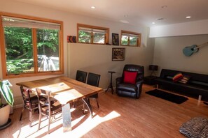 A modern living room with a wooden dining table, black leather sofa, and a guitar wall decoration.