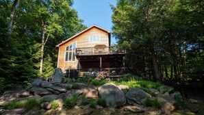 Une cabane en bois dotée d’un balcon, entourée d’une forêt et de grands rochers.