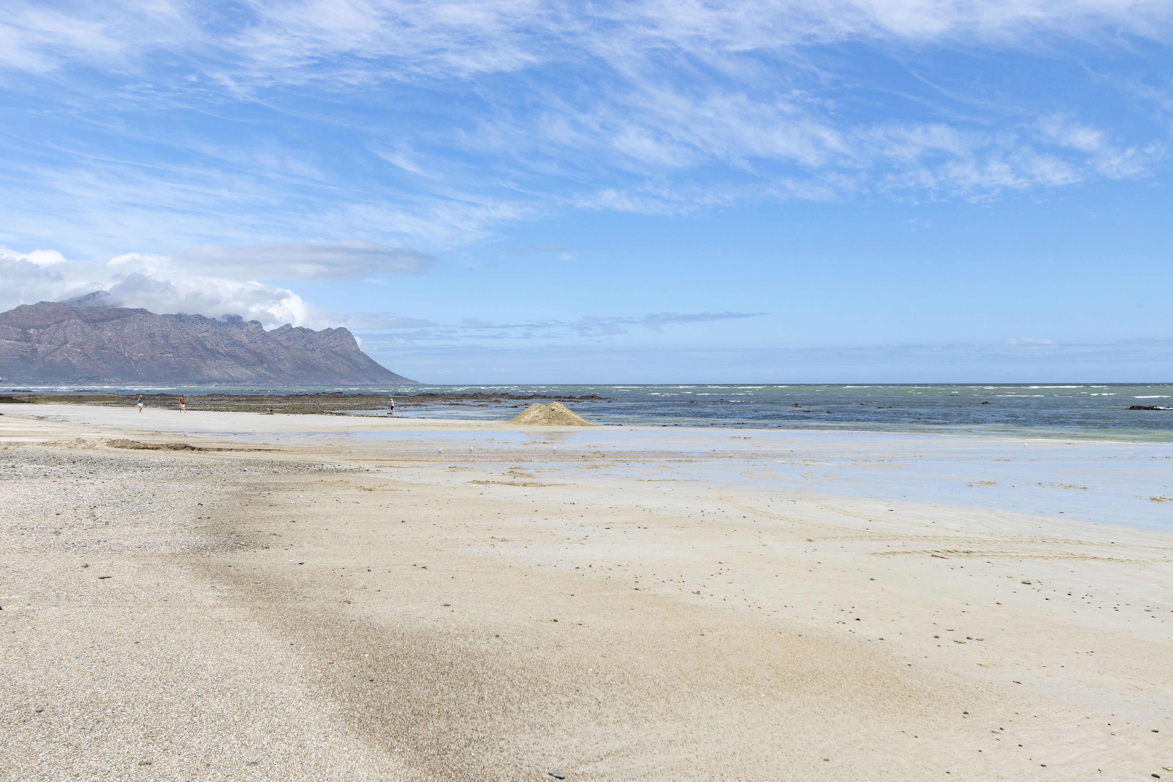 A beach with a mountain in the background, clear skies, and calm sea.