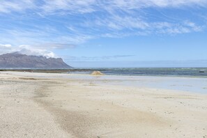 En strand med et bjerg i baggrunden, klare himmel og roligt hav.