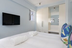 A bedroom with a bed, a TV mounted on the wall, a wardrobe, and a window.