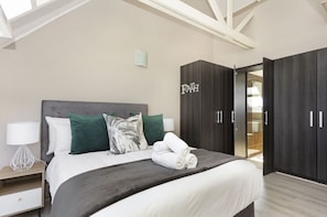 A modern bedroom with a large bed, dark wooden wardrobe, and a nightstand with a lamp. - Dolphin Beach H301 (Cape Town)