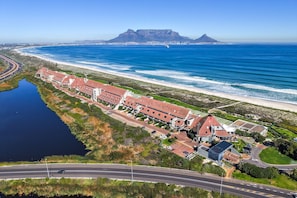 An aerial view of a coastal hotel with multiple buildings, a road, and a beach. - Dolphin Beach H301 (Cape Town)