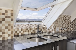 A kitchen with a checkered tile backsplash, a skylight, and a view of distant mountains. - Dolphin Beach H301 (Cape Town)