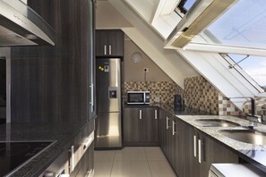 A modern kitchen with dark wood cabinets, stainless steel appliances, a microwave, and a skylight. - Dolphin Beach H301 (Cape Town)