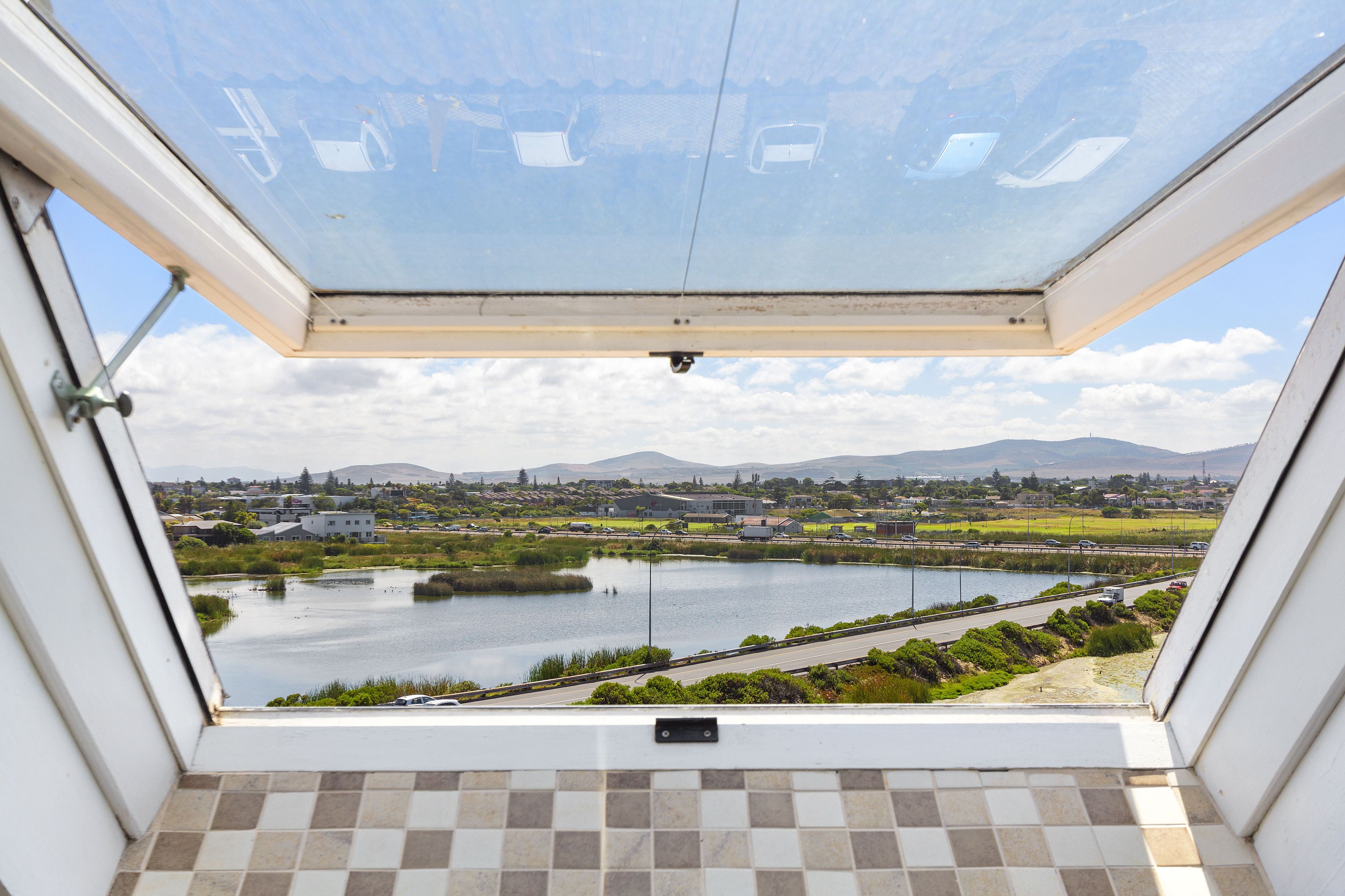 A view from a room with a large window overlooking a lake, a road, and distant hills.
