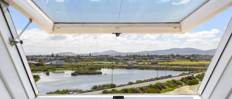 A view from a room with a large window overlooking a lake, a road, and distant hills.