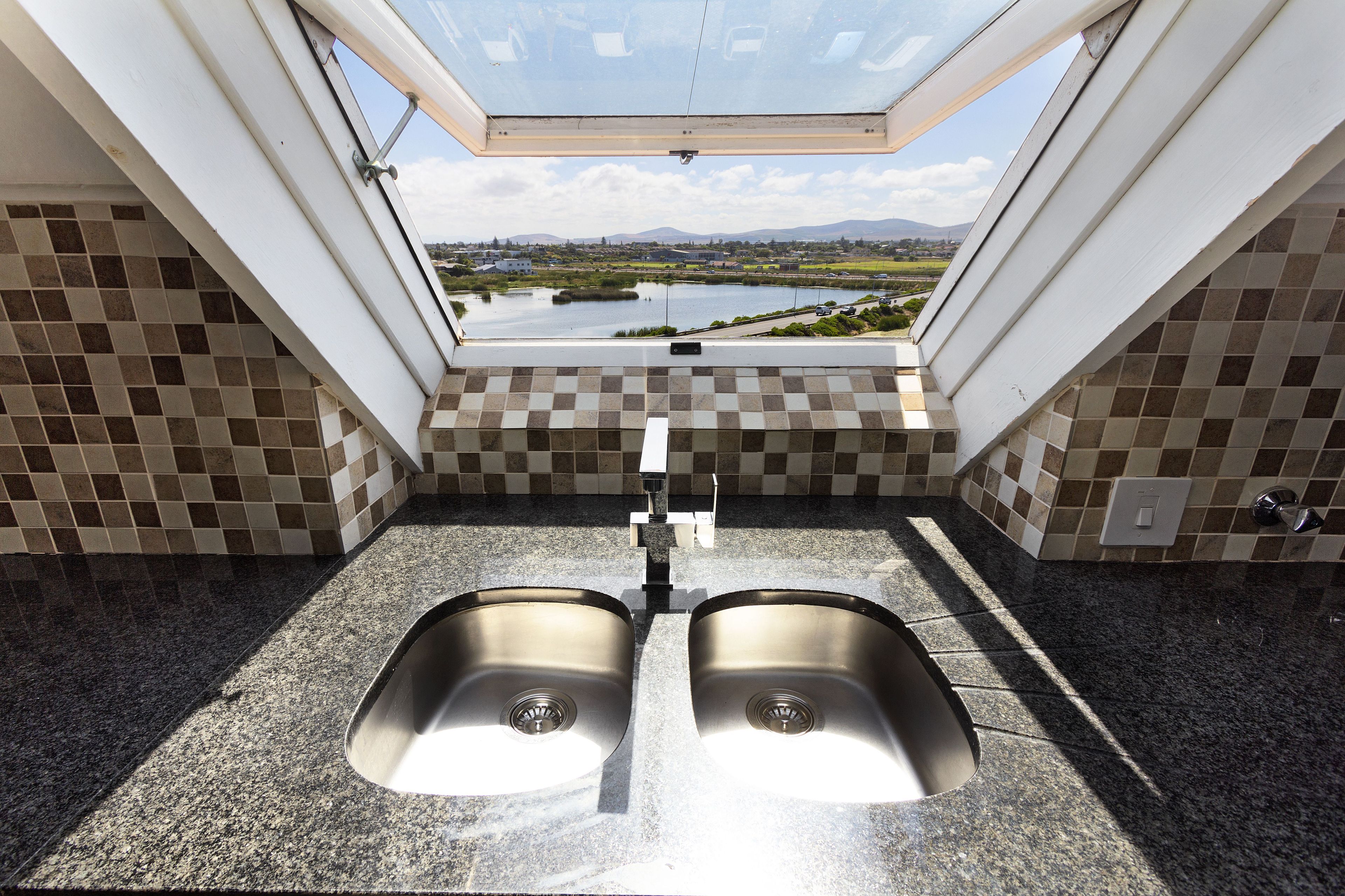 A kitchen with two stainless steel sinks, a window with a view of a lake and mountains, and checkered tile walls.