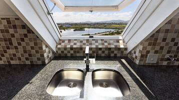 A kitchen with two stainless steel sinks, a window with a view of a lake and mountains, and checkered tile walls.