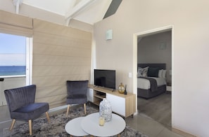A modern living room with a TV, two armchairs, a coffee table, and a view of the sea. - Dolphin Beach H301 (Cape Town)