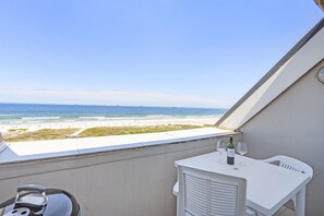 A balcony with a view of the beach and ocean, a white table with a bottle of wine and glasses, and a white chair. - Dolphin Beach H301 (Cape Town)