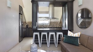 Una cocina moderna con una isla central, taburetes de bar y un área de comedor con sofá y cojines.