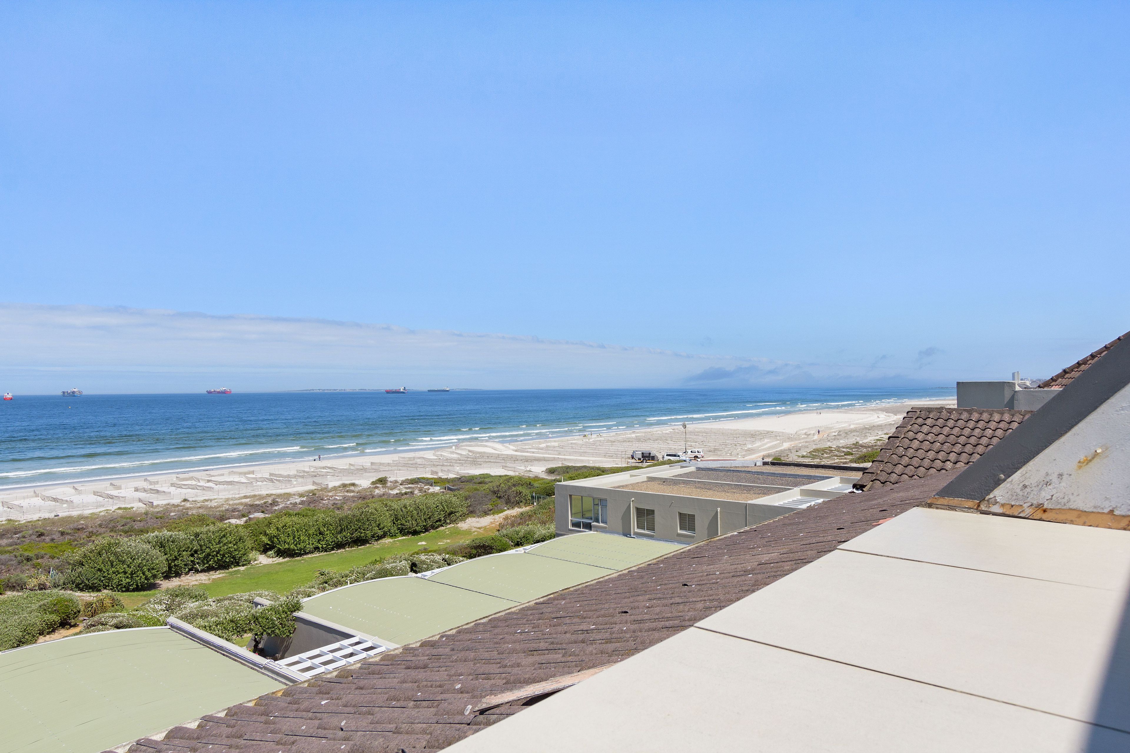 Une terrasse sur le toit offrant une vue sur la plage et l’océan, agrémentée d’un toit végétalisé et d’un mur blanc.