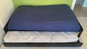 Uma cama com colchão azul e lençol de proteção branco em um quarto com paredes verdes e piso de azulejos.