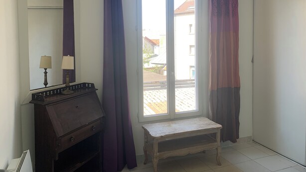 Quarto com janela, um banco e cômoda de madeira com luminárias.