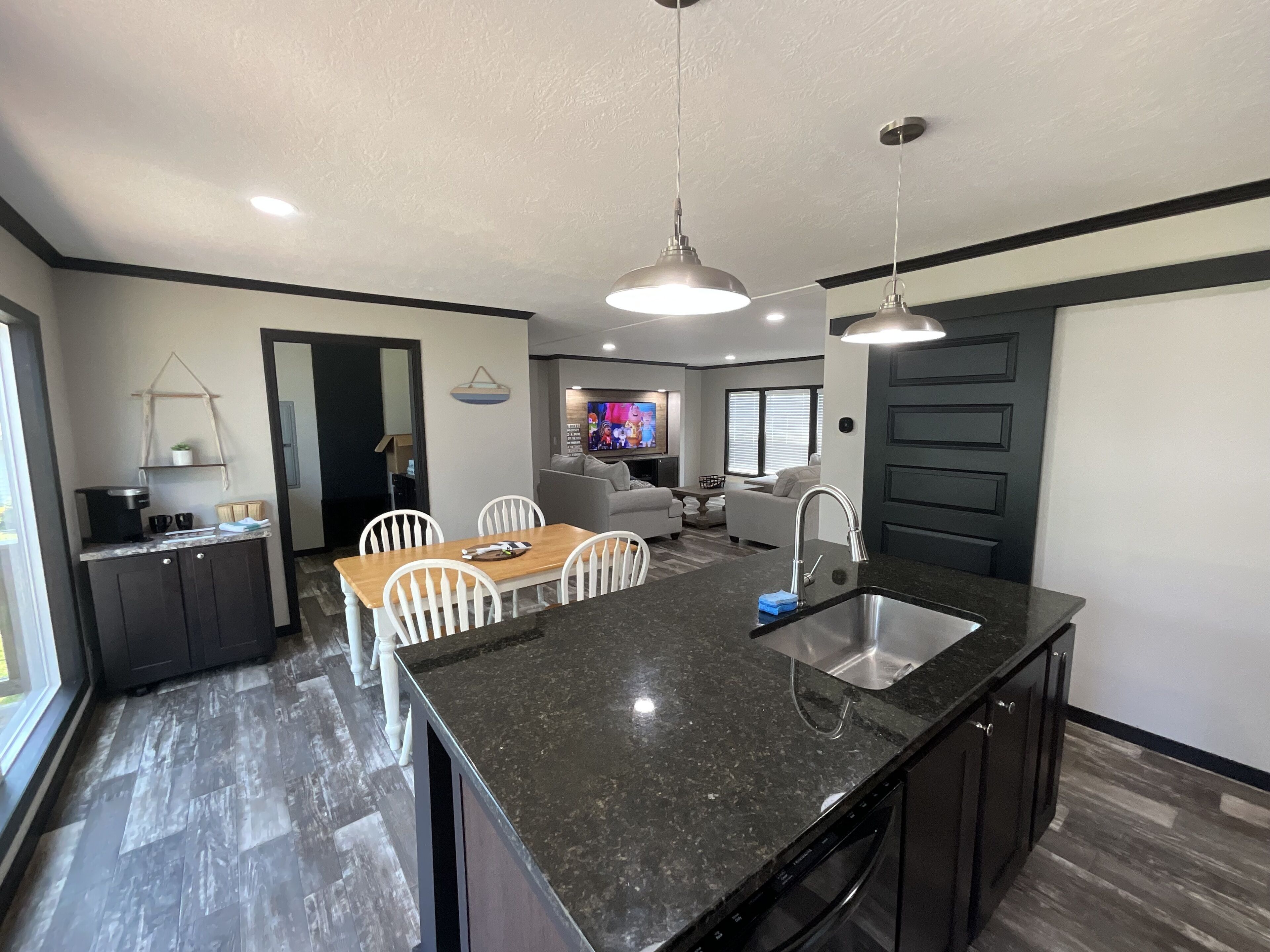 A modern kitchen with a large island, dark countertops, and a built-in dishwasher.