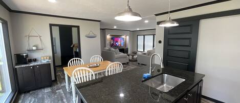 A modern kitchen with a large island, dark countertops, and a built-in dishwasher.