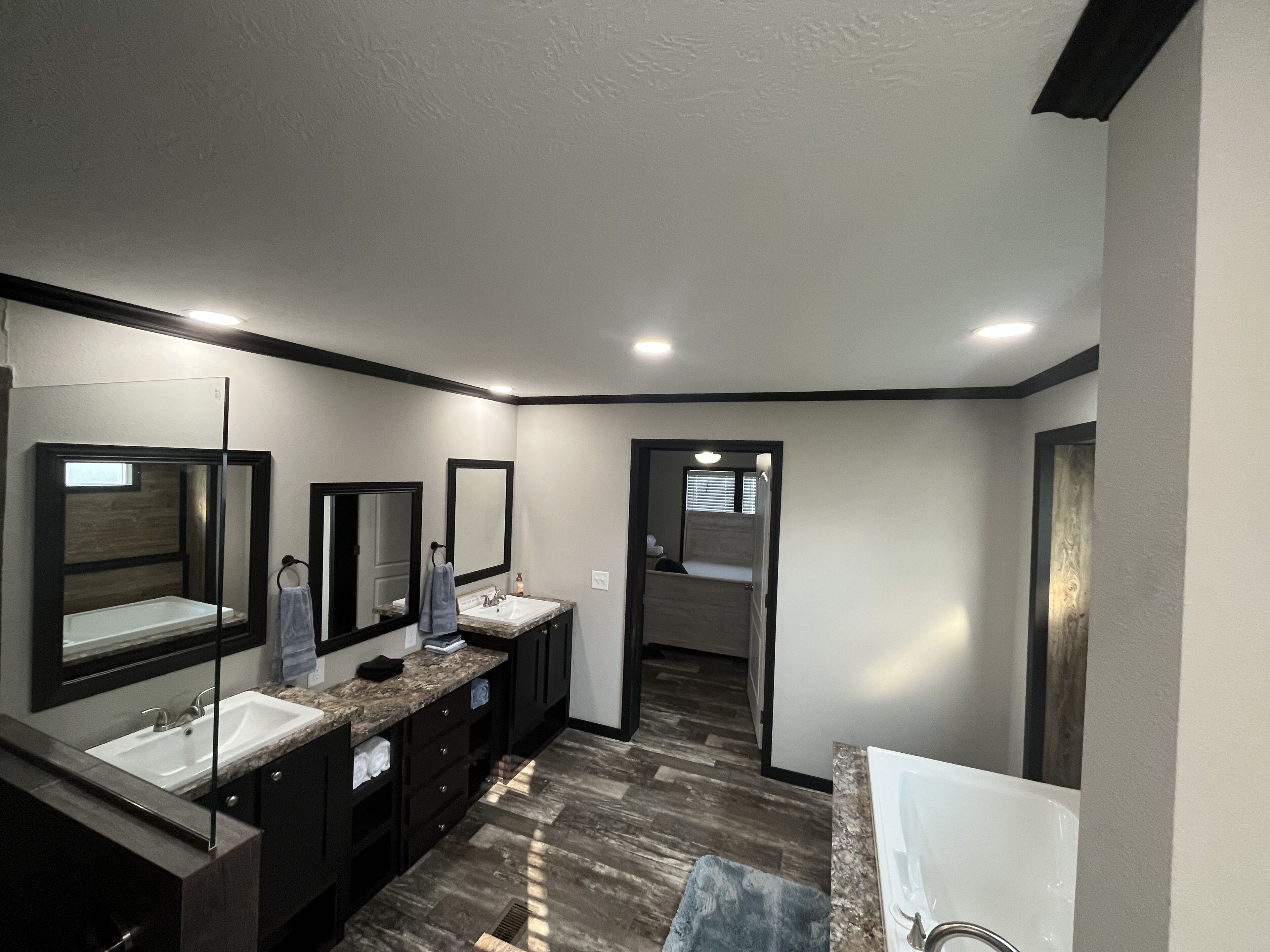 Un baño moderno con un espejo grande, dos lavamanos, muebles oscuros y una zona de ducha.