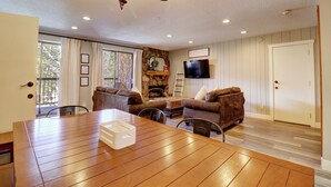 A living room with a wooden dining table, two brown leather sofas, a fireplace, and a television mounted on the wall. - Dog Friendly, Ski In/Ski Out Condo, Perfect Location, High Capacity CM325 (Copper Mountain)