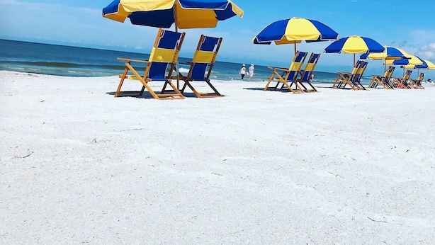 Strandliegen und Sonnenschirme auf einem Sandstrand, im Hintergrund das Meer.