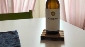 Une bouteille de vin de Cormons posée sur un sous-verre en bois, sur une table blanche.