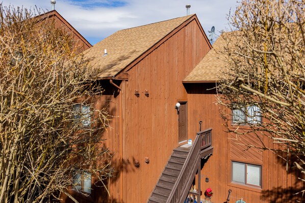 A wooden building with a staircase leading to a door, surrounded by trees.