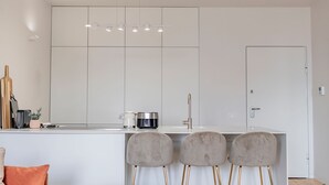 A modern kitchen with white cabinets, a stainless steel sink, and a bar area with three bar stools. - Almada 551 - 3.1 l Luxury Living by LovelyStay (Porto)