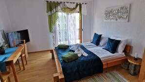 Une chambre à coucher avec un lit, un bureau, une chaise, une télévision et une fenêtre avec des rideaux.
