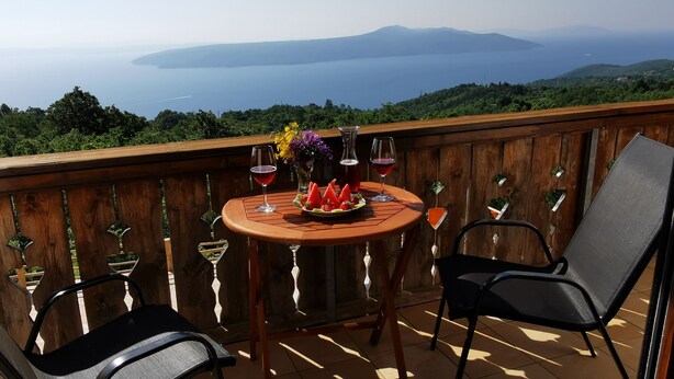 Une terrasse en bois avec une table ronde et deux chaises, offrant une vue panoramique sur un lac et des montagnes.