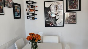Et spiseområde med et hvidt bord, stole, en vase med orange blomster, et vægur og billeder i rammer.