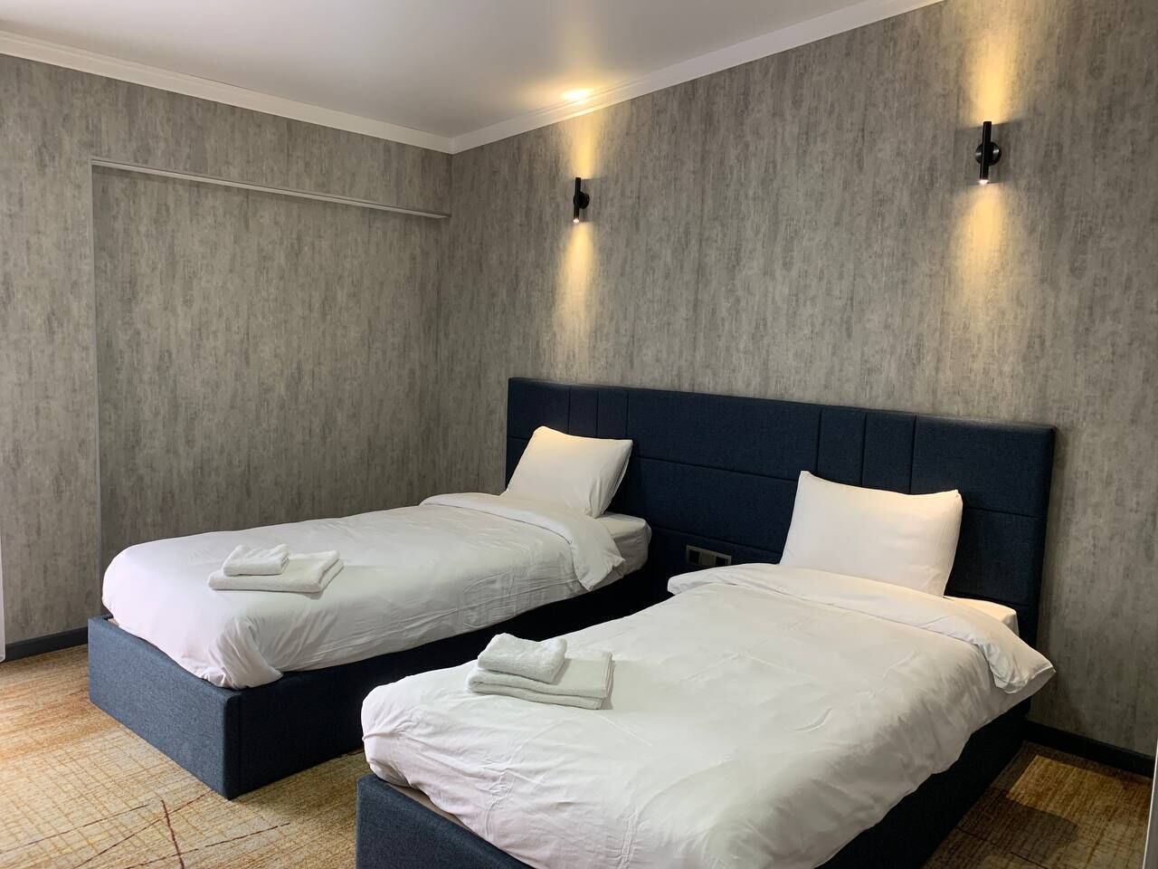 A hotel room with two single beds, each with a dark headboard and white bedding.