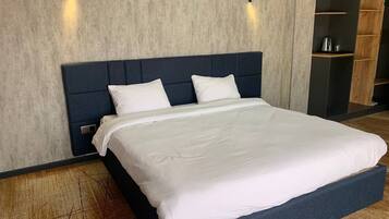 A modern hotel room with a large bed, a dark headboard, and built-in shelves with a coffee maker.