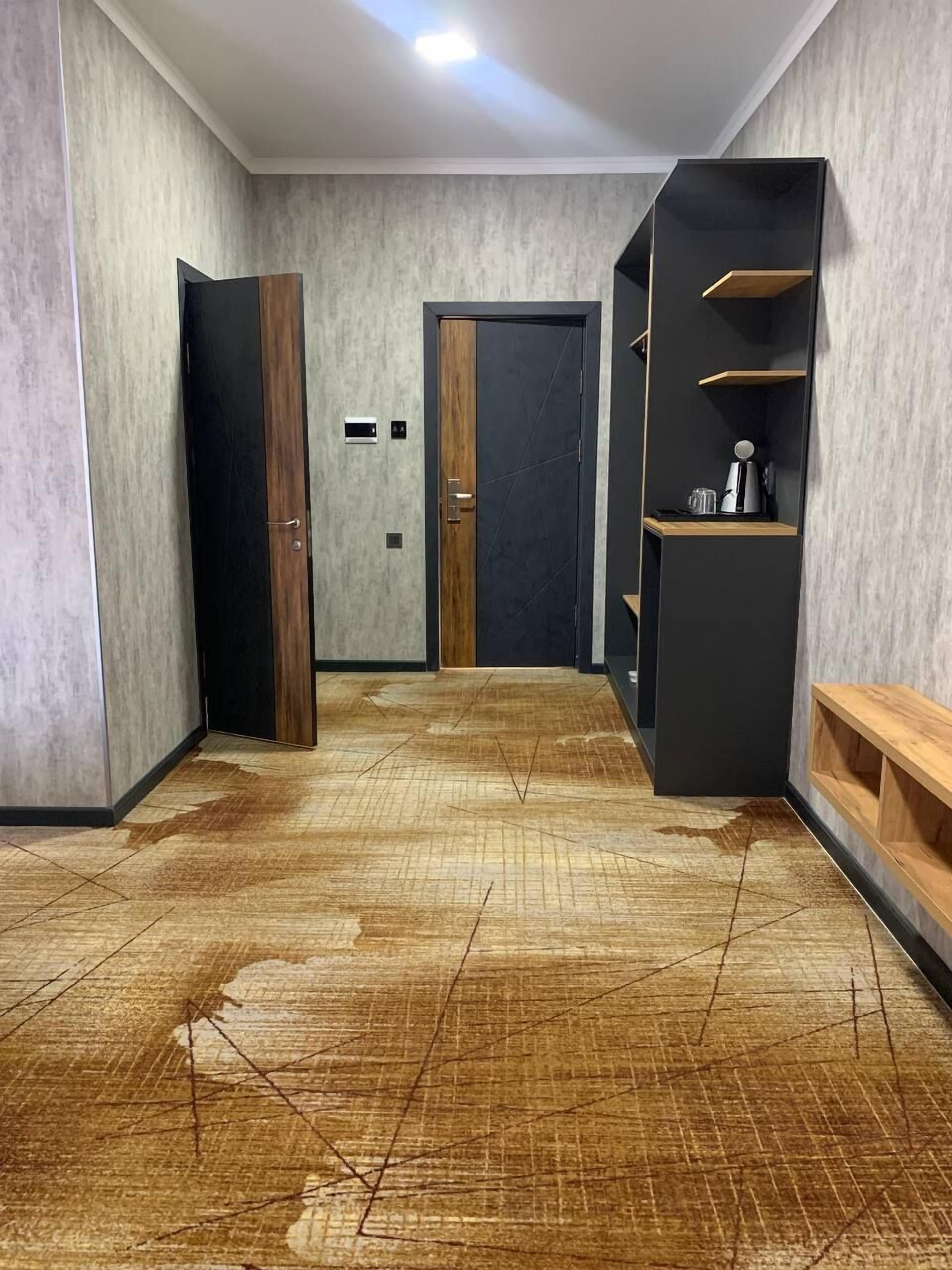 Un corridoio con pavimento in legno, una porta nera e un mobile contenitore nero con una macchina per caffè.