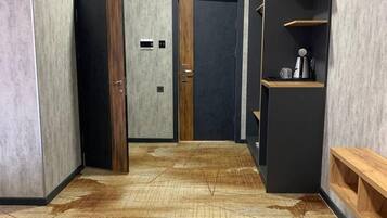 Un corridoio con pavimento in legno, una porta nera e un mobile contenitore nero con una macchina per caffè.