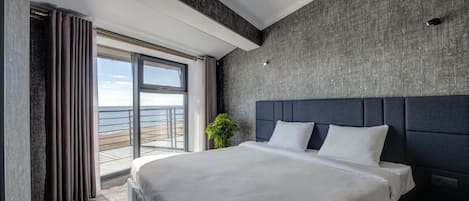 A modern hotel room with a large bed, a view of the sea, and a balcony with curtains.