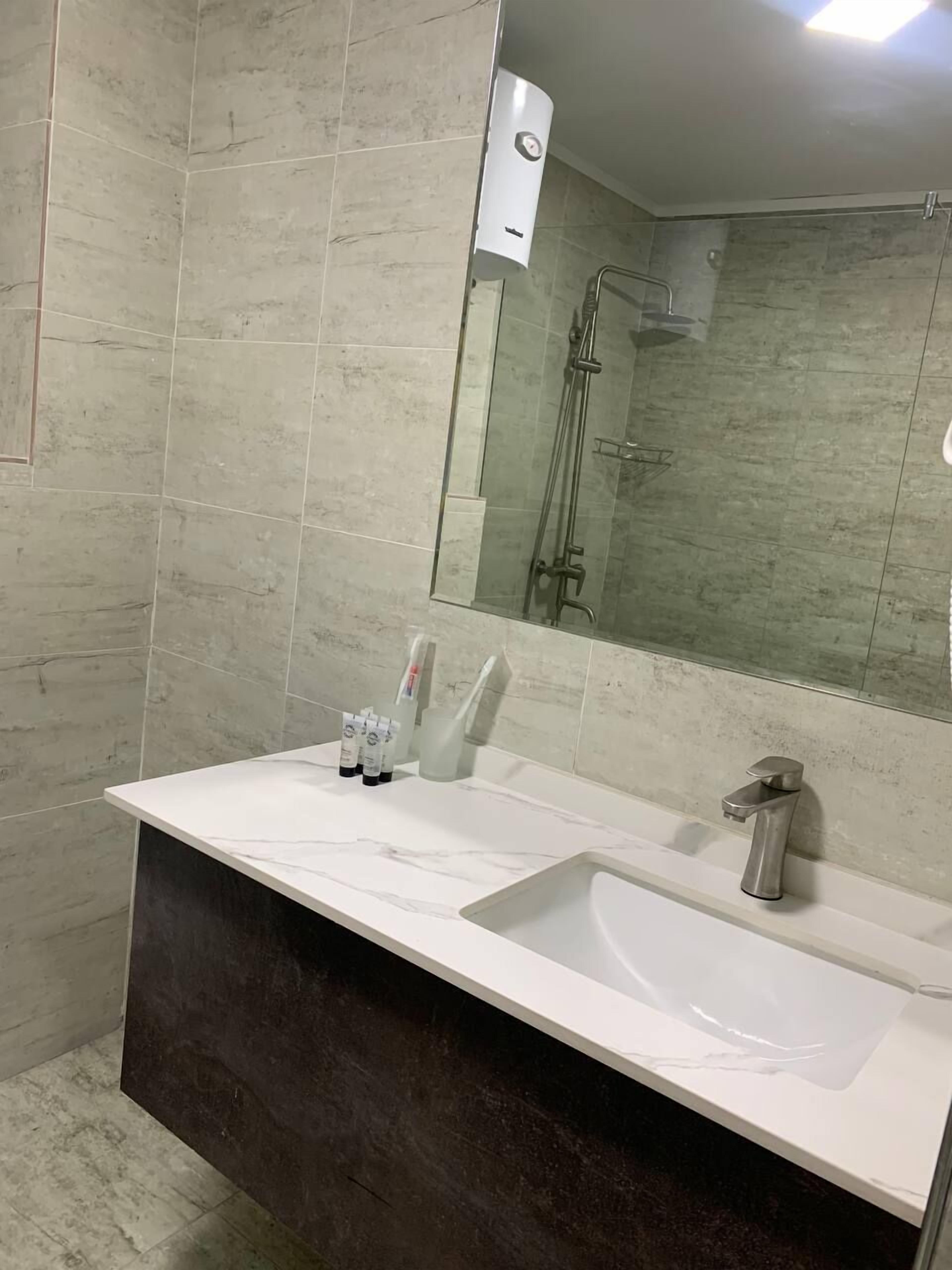 Een moderne badkamer met een grote spiegel, een witte wastafel en een douche.