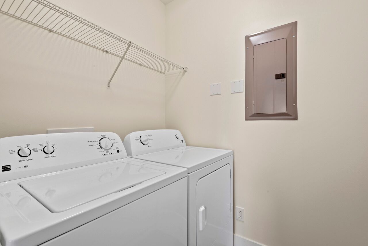A laundry area with a front-loading washer and dryer, a metal drying rack, and a door with a handle.