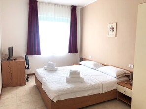 A hotel room with a bed, a desk with a computer, a bedside table, and a window with curtains. - Sportland (Colle di Val d'Elsa)