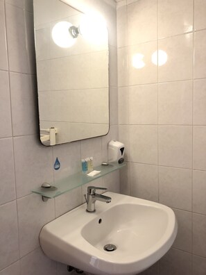 A bathroom with a white sink, a glass shelf with toiletries, and a mirror. - Sportland (Colle di Val d'Elsa)