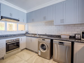A modern kitchen with white cabinets, a stainless steel dishwasher, a built-in oven, and a washing machine.