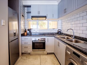 A compact kitchen with white cabinets, a stainless steel refrigerator, a built-in oven, a dishwasher, and a washing machine.