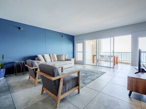 Ett modernt vardagsrum med en blå accentvägg, en soffa, två fåtöljer, ett soffbord och en tv.