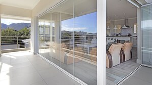 A spacious balcony with a modern sliding glass door leading to a dining area with a kitchen in the background. - Ocean View Family Beach House (Hermanus)