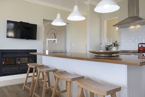 A modern kitchen with a wooden island, bar stools, pendant lights, and a flat-screen TV.