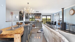 Uma cozinha moderna com uma ilha central, uma área de jantar com mesa de madeira e cadeiras estofadas em cinza, e uma grande janela com vista para o exterior.
